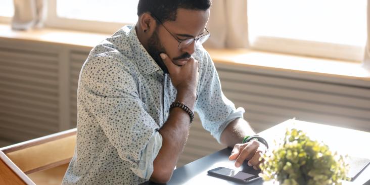 Man sitting at a desk looking thoughtfully at a cell phone